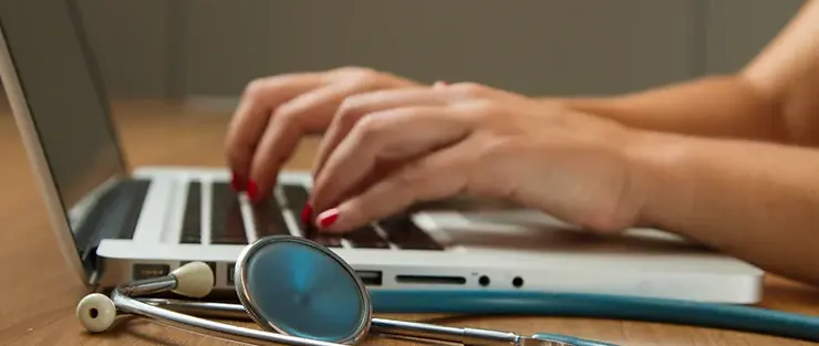 Hands typing on laptop with stethoscope